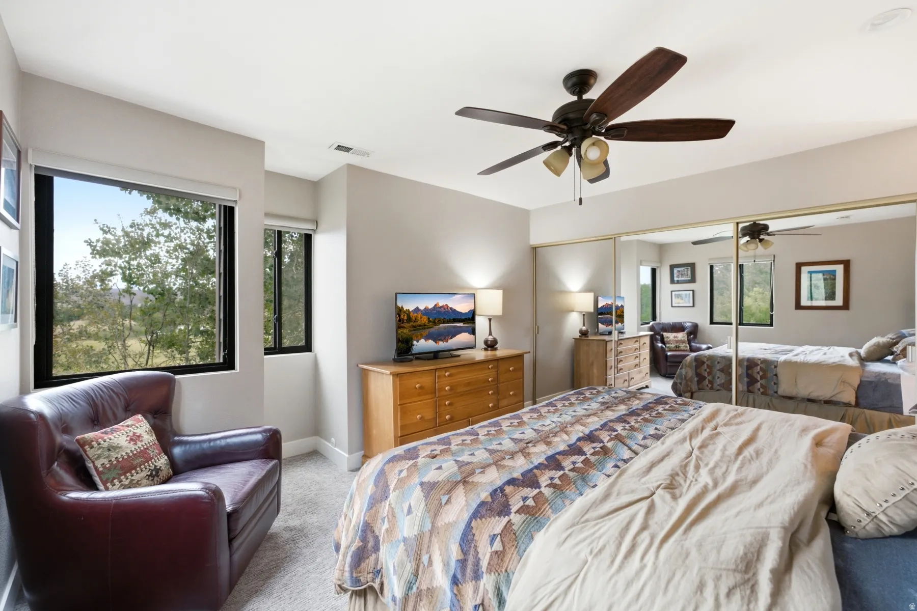 Bedroom featuring multiple windows, a ceiling fan with integrated lighting, mirrored closet doors, and light-toned wall paint