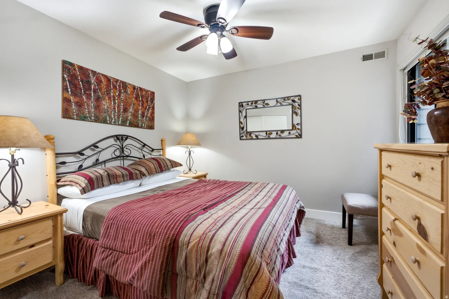 Carpeted room featuring a ceiling fan with integrated lighting, a window with trim, light-toned walls, and a built-in ventilation register