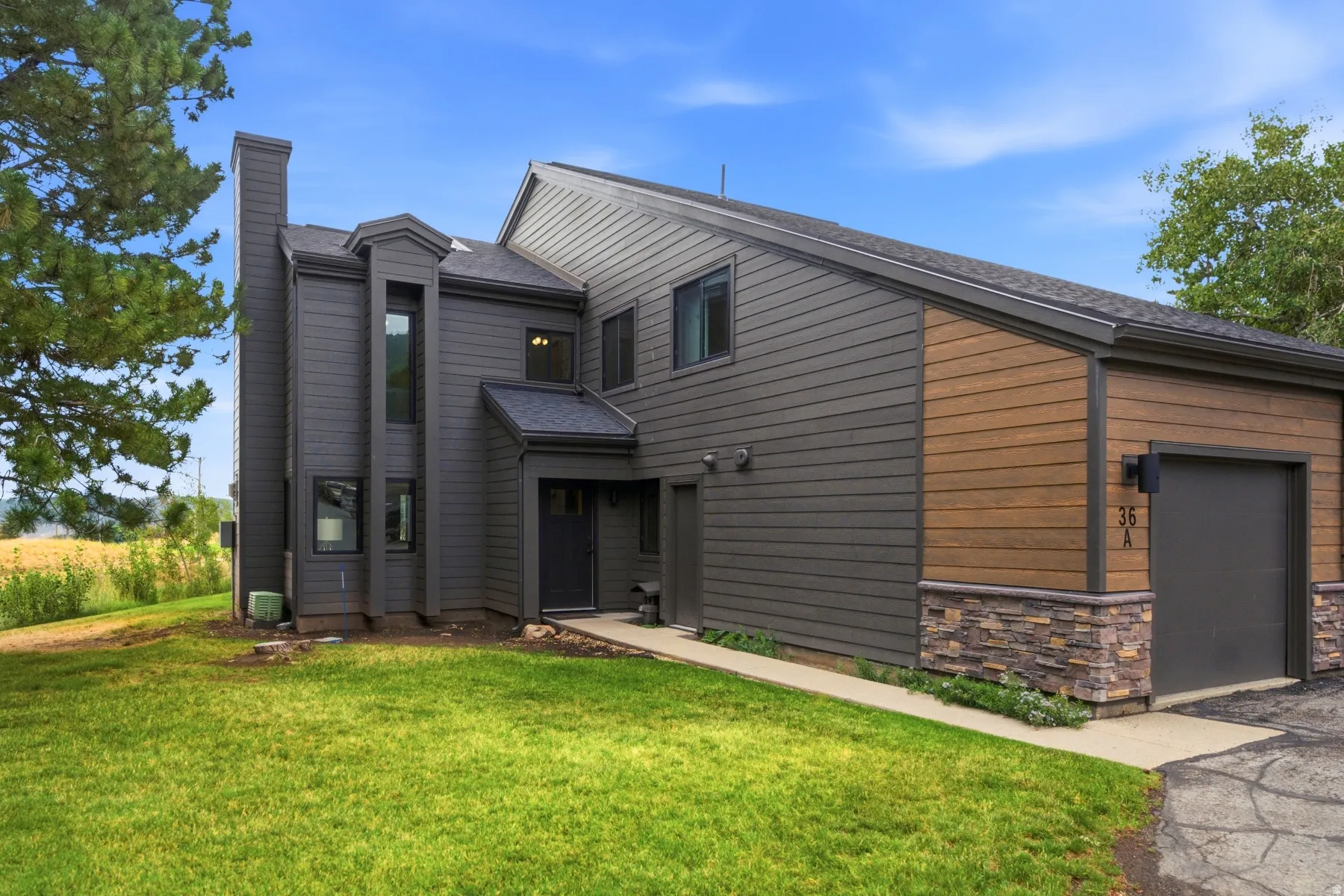 Contemporary exterior featuring dark gray siding, wood-finish accent panels, stacked stone detailing, and an integrated single-car garage