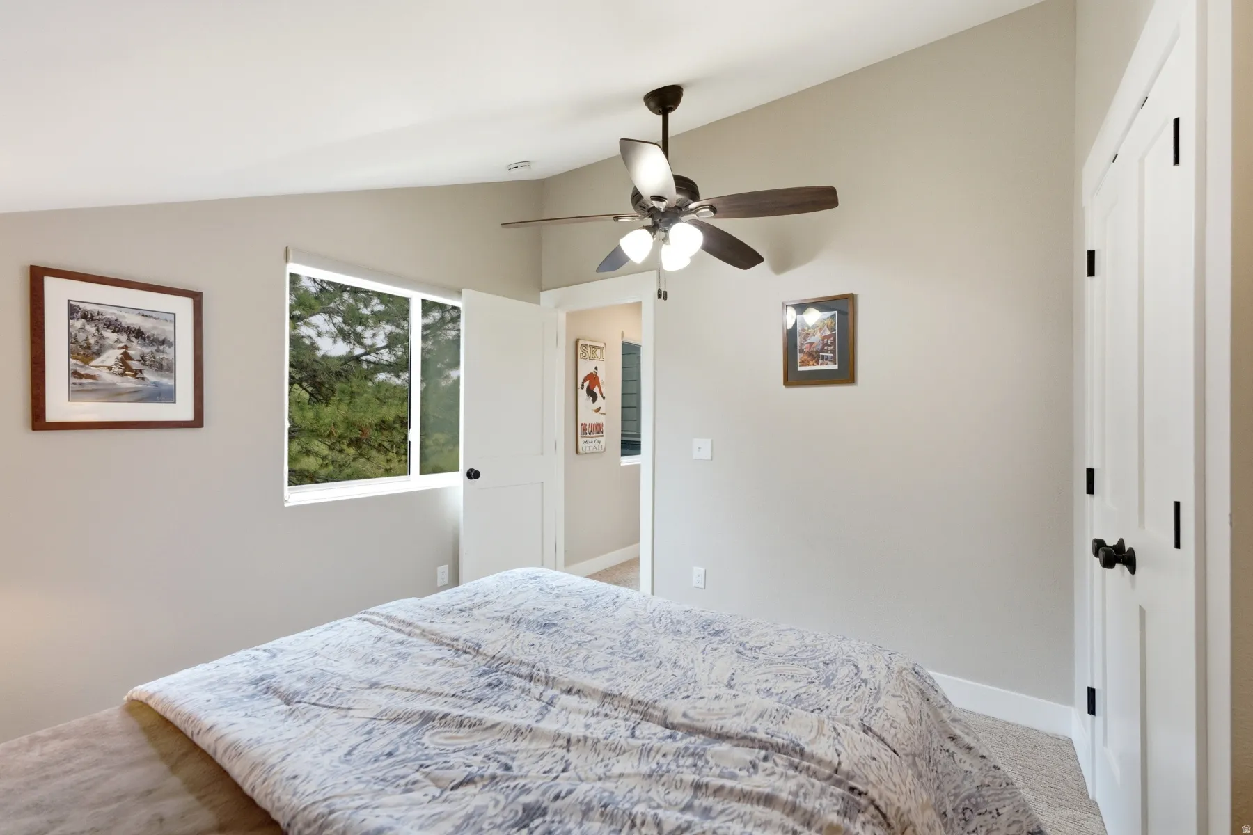 Vaulted ceiling room featuring a ceiling fan with light fixture, large window, and white panel doors with black hardware