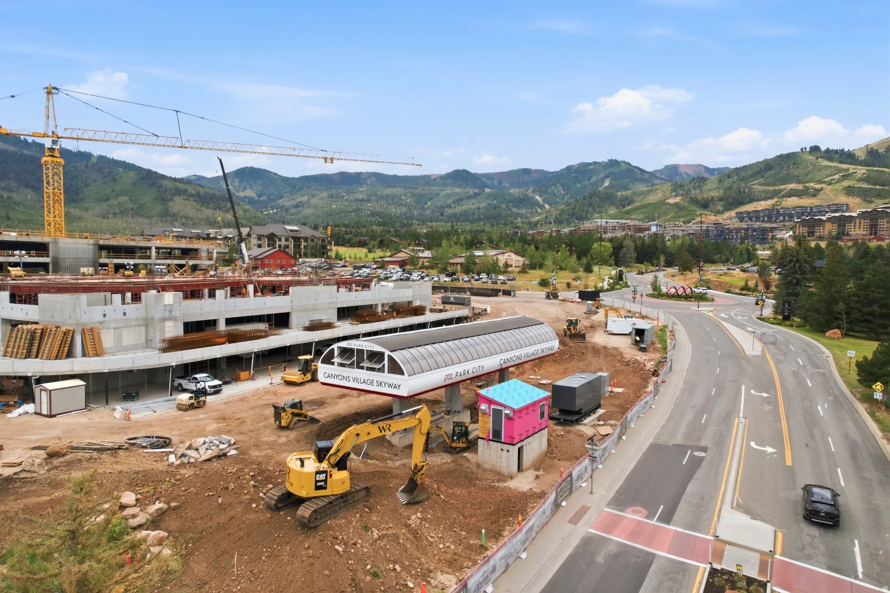 Canyons Village Skyway station with surrounding construction, a multi-lane paved road, mountain backdrop, and wooded terrain