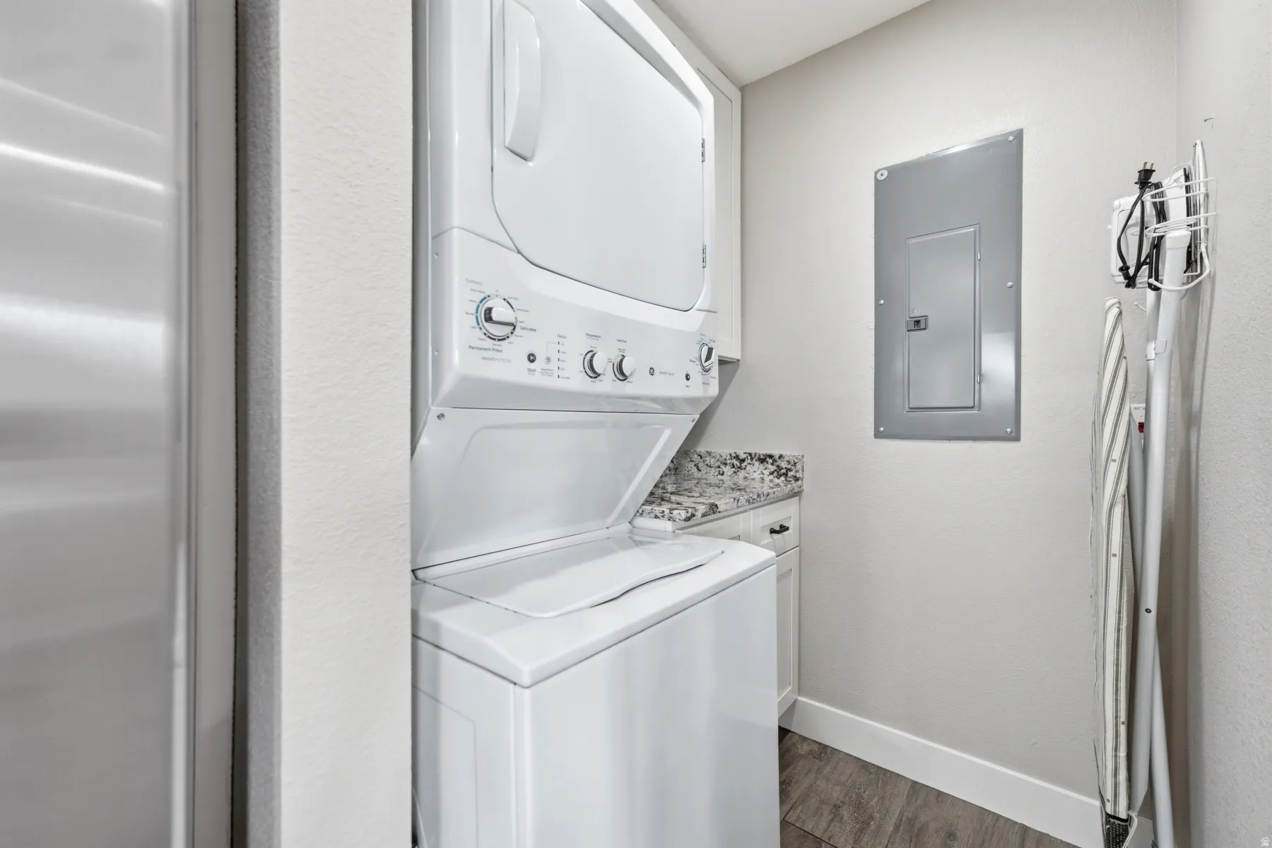Dedicated laundry area featuring a stacked washer and dryer, light-colored cabinetry with a stone-finish countertop, and wood-finish flooring