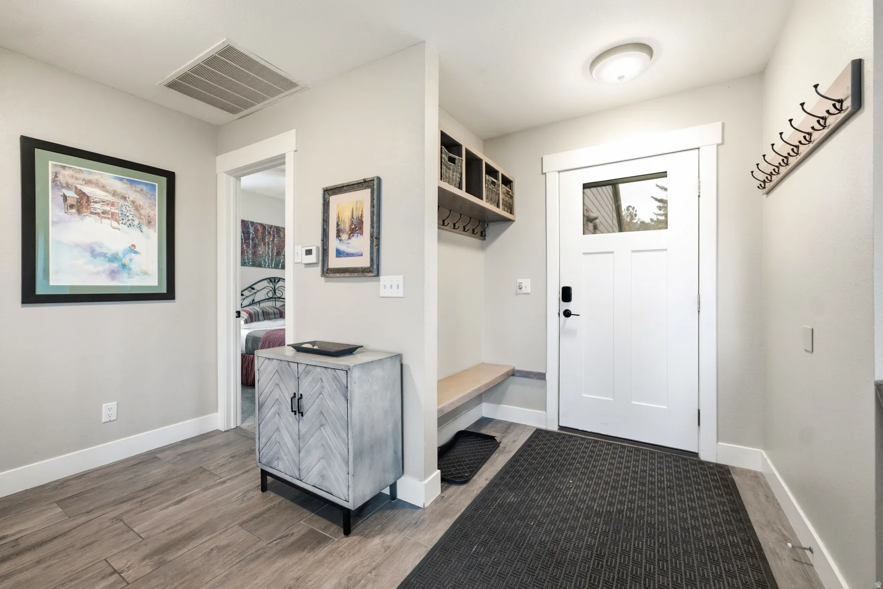 Entryway featuring wood-finish flooring, a white paneled door with a transom window, a built-in bench, and an integrated coat rack with cubbies