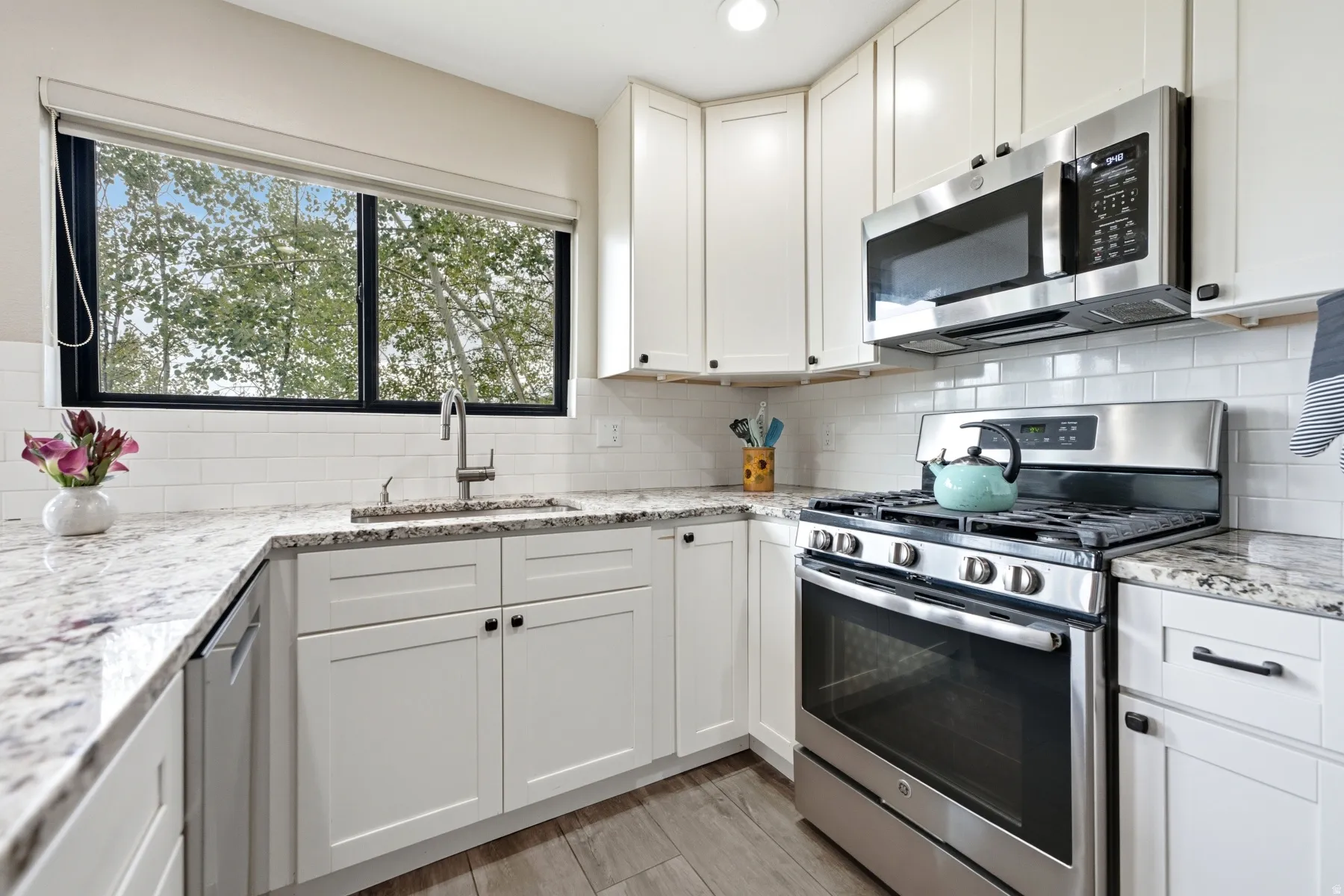 Well-appointed kitchen featuring white cabinetry, light-toned countertops, a stainless steel gas range, and a stainless steel microwave above