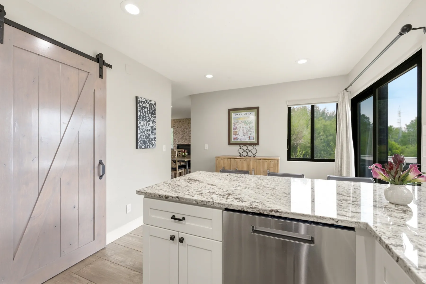 Kitchen featuring a large island with a speckled stone countertop, white shaker cabinetry, and a built-in stainless steel dishwasher