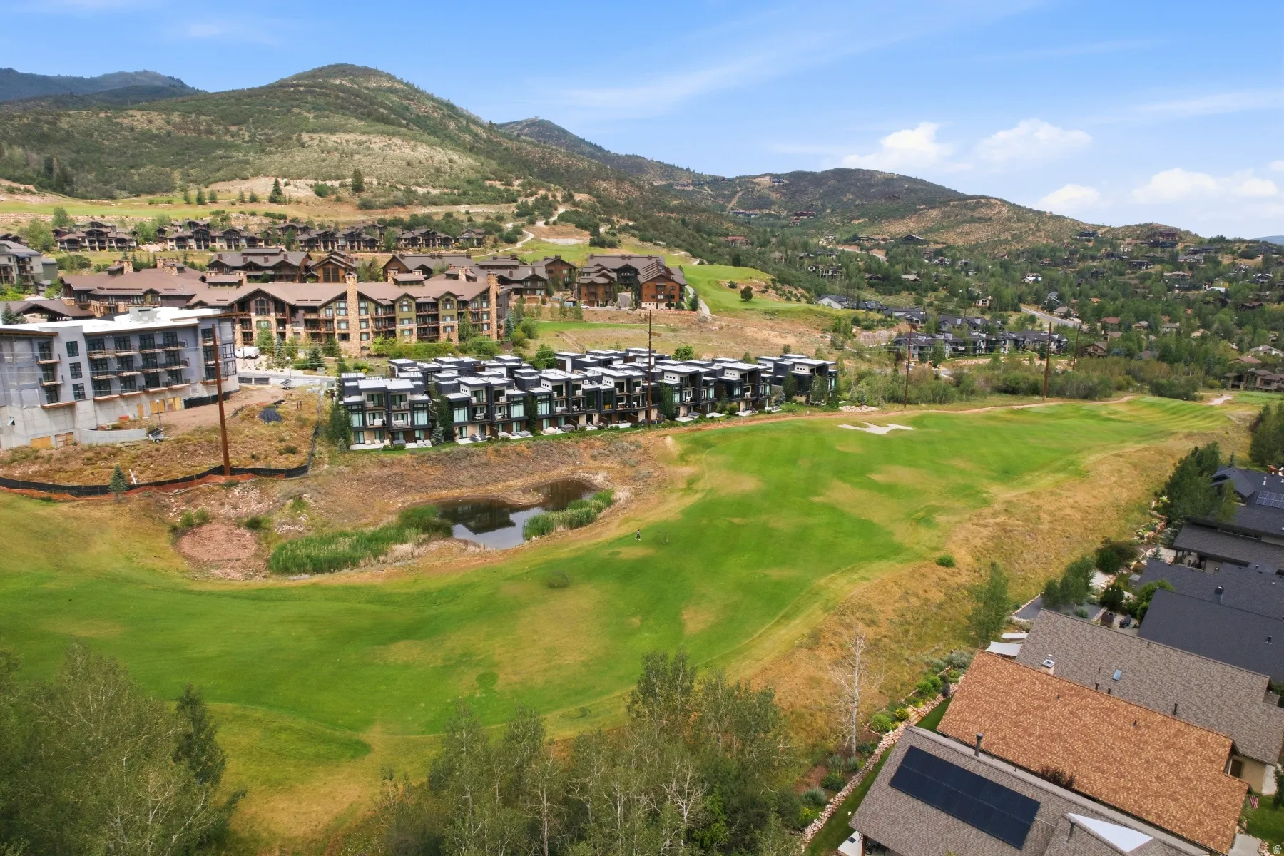 Expansive golf course landscape featuring a water hazard, surrounded by multi-level residential buildings with varied architectural styles