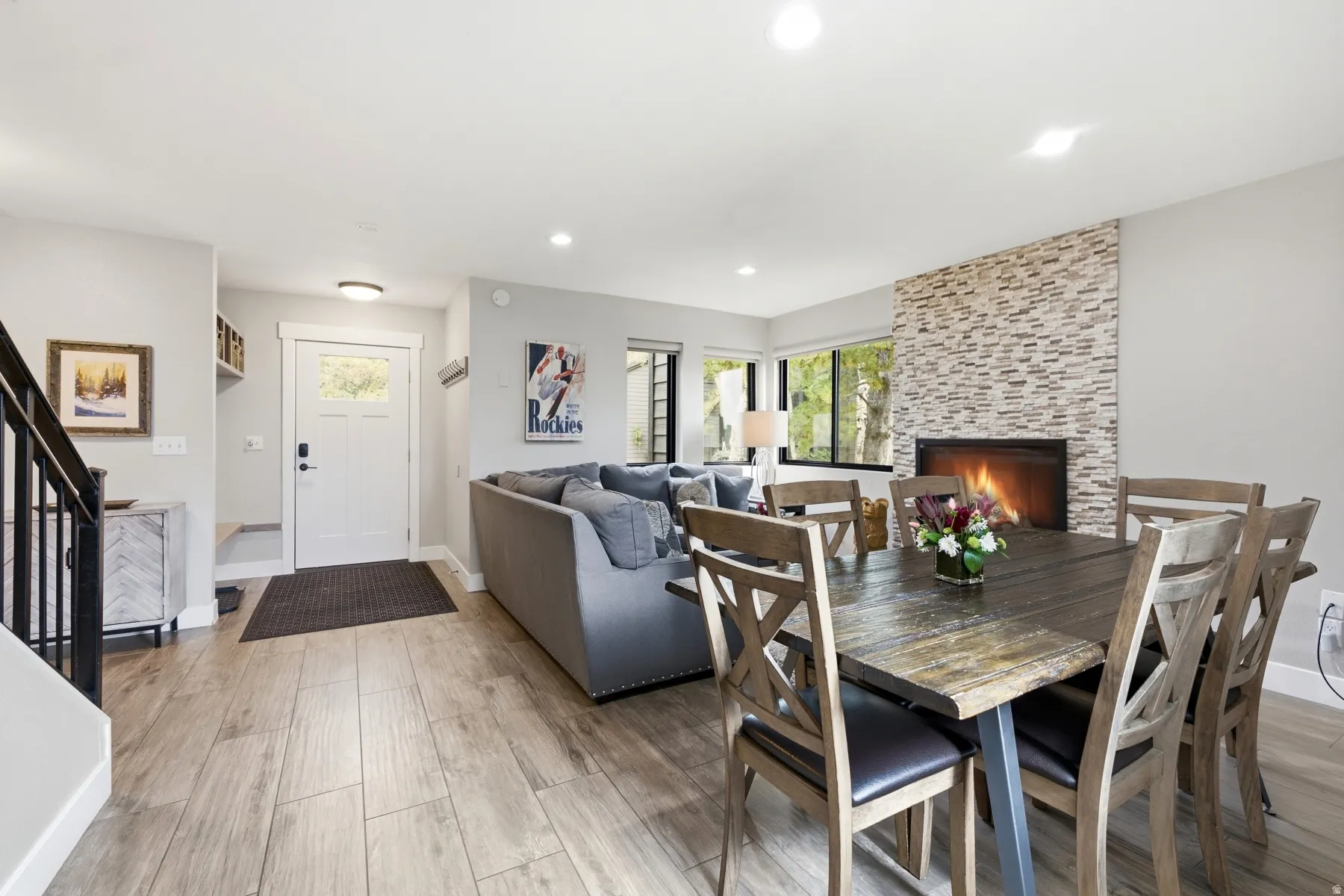 Open-concept living area with wood-finish flooring, a stone-clad fireplace, and recessed lighting