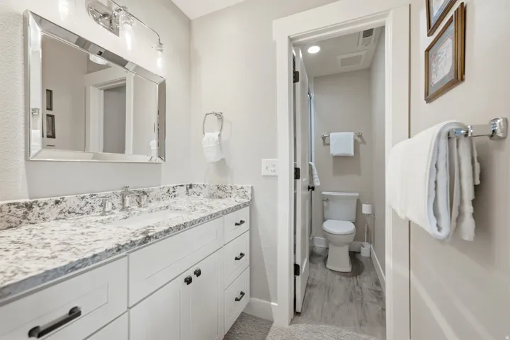 White shaker-style vanity with a granite countertop, undermount sink, and chrome faucet