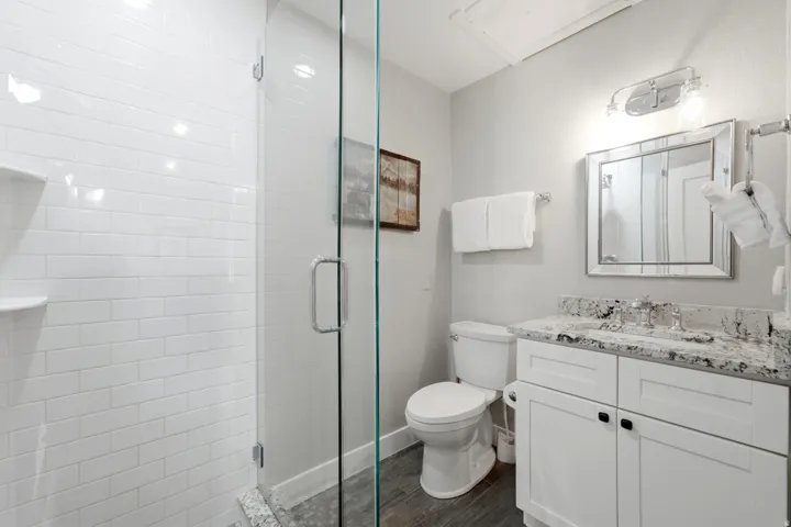 Contemporary bathroom featuring a frameless glass shower enclosure, white subway tile shower surround, and wood-finish flooring