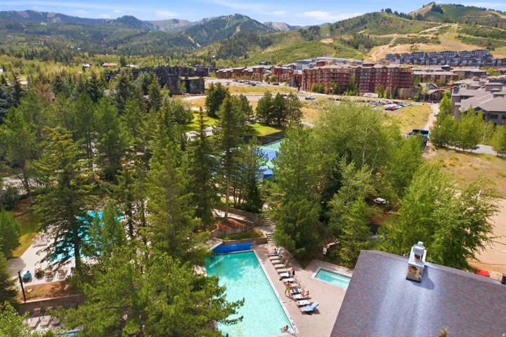 Expansive outdoor amenity area featuring multiple swimming pools, a hot tub, and a tennis court, all surrounded by mature evergreen trees