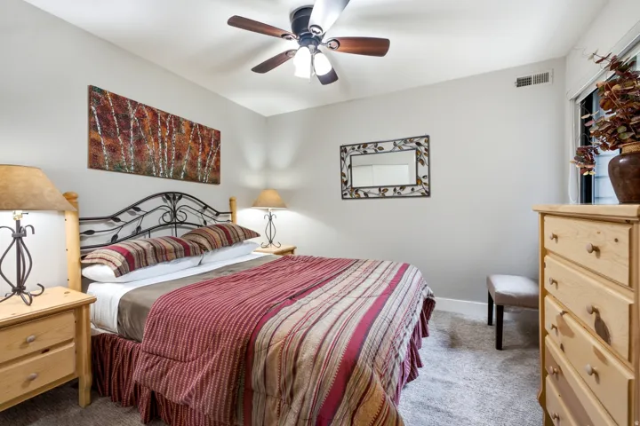 Carpeted room featuring a ceiling fan with integrated lighting, a window with trim, light-toned walls, and a built-in ventilation register