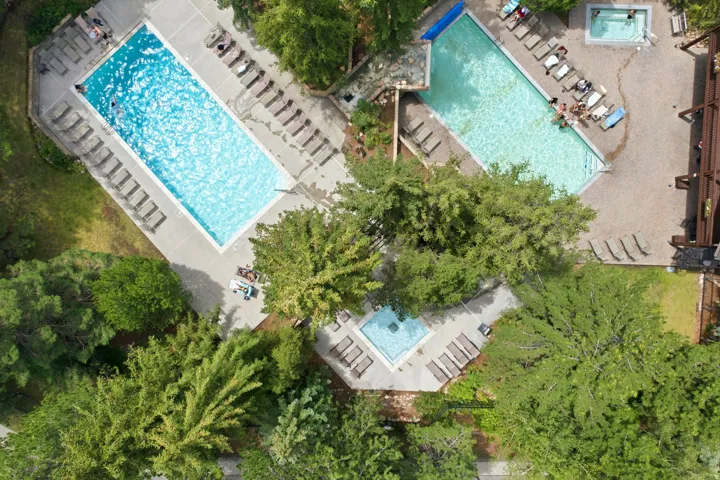 Outdoor amenity area featuring two swimming pools, two spas, extensive concrete and gravel decking, and mature landscaping