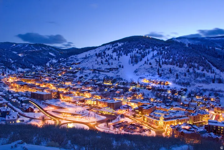 Expansive mountain town featuring illuminated buildings, snow-covered terrain, and surrounding forested slopes