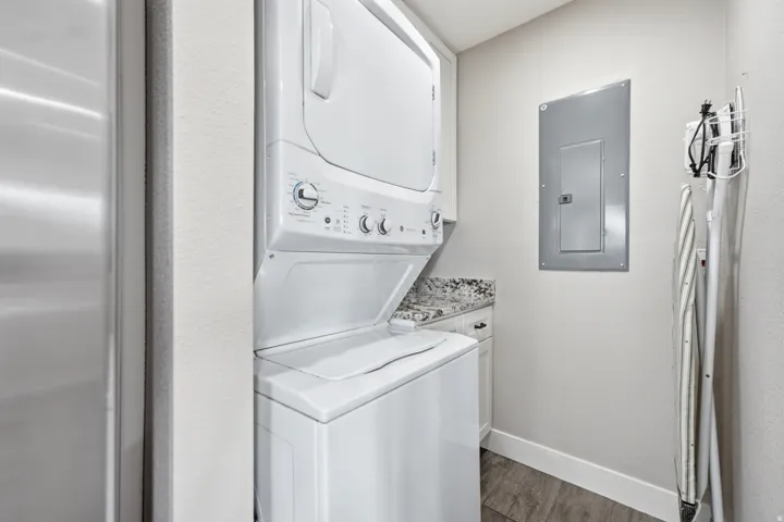 Dedicated laundry area featuring a stacked washer and dryer, light-colored cabinetry with a stone-finish countertop, and wood-finish flooring