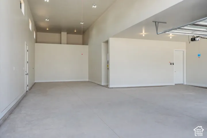 Spacious garage featuring a concrete floor, high ceilings, multiple doors for access, and overhead lighting
