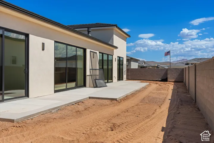 Rear exterior featuring a large concrete patio, multiple sliding glass doors, exterior wall sconces, and stucco siding
