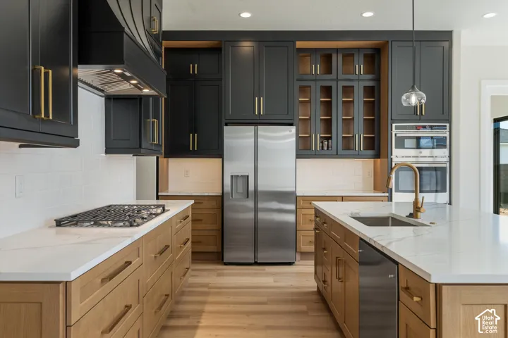 Gourmet kitchen featuring a built-in gas range, stainless steel appliances, a center island with sink, and two-tone cabinetry with gold-finish hardware