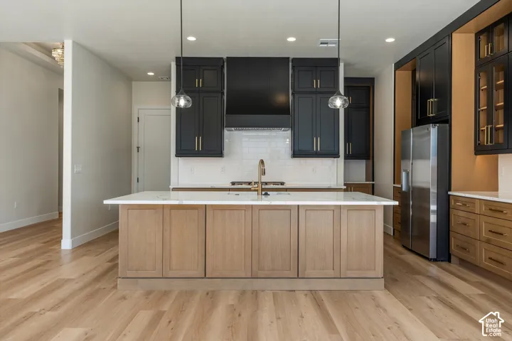 Kitchen island with stone countertop, wood-finish flooring, matte black cabinetry with gold-tone hardware, stainless steel refrigerator, and pendant lighting