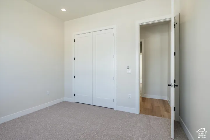 Recessed lighting, light-toned carpeting, white trim, and a white bi-fold closet door with black hardware