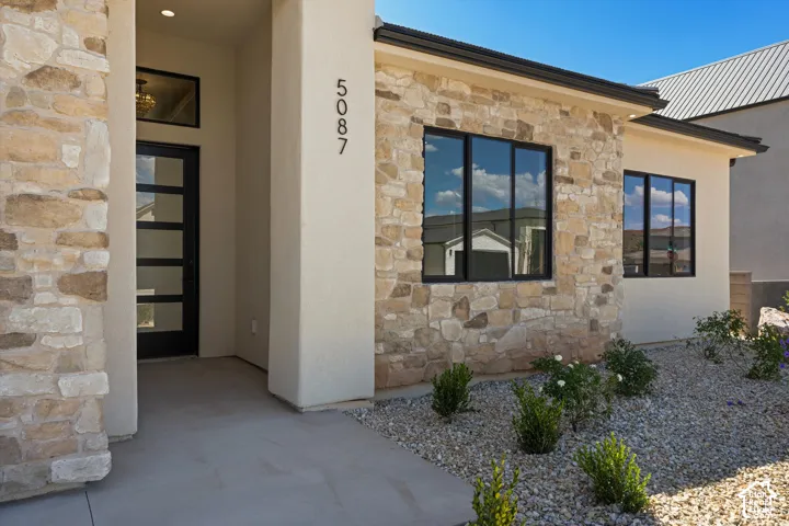 Stone-clad exterior with stucco accents, modern black-framed windows, a contemporary entry door with frosted glass panels, and a low-maintenance gravel landscape