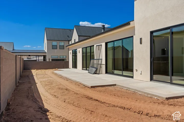 Modern residence featuring an expansive rear patio with polished concrete decking, floor-to-ceiling sliding glass doors with black aluminum framing, and direct access to a generous landscaped yard
