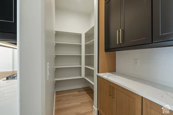 Walk-in pantry with extensive shelving, wood-finish flooring, white subway tile backsplash, and stone countertops