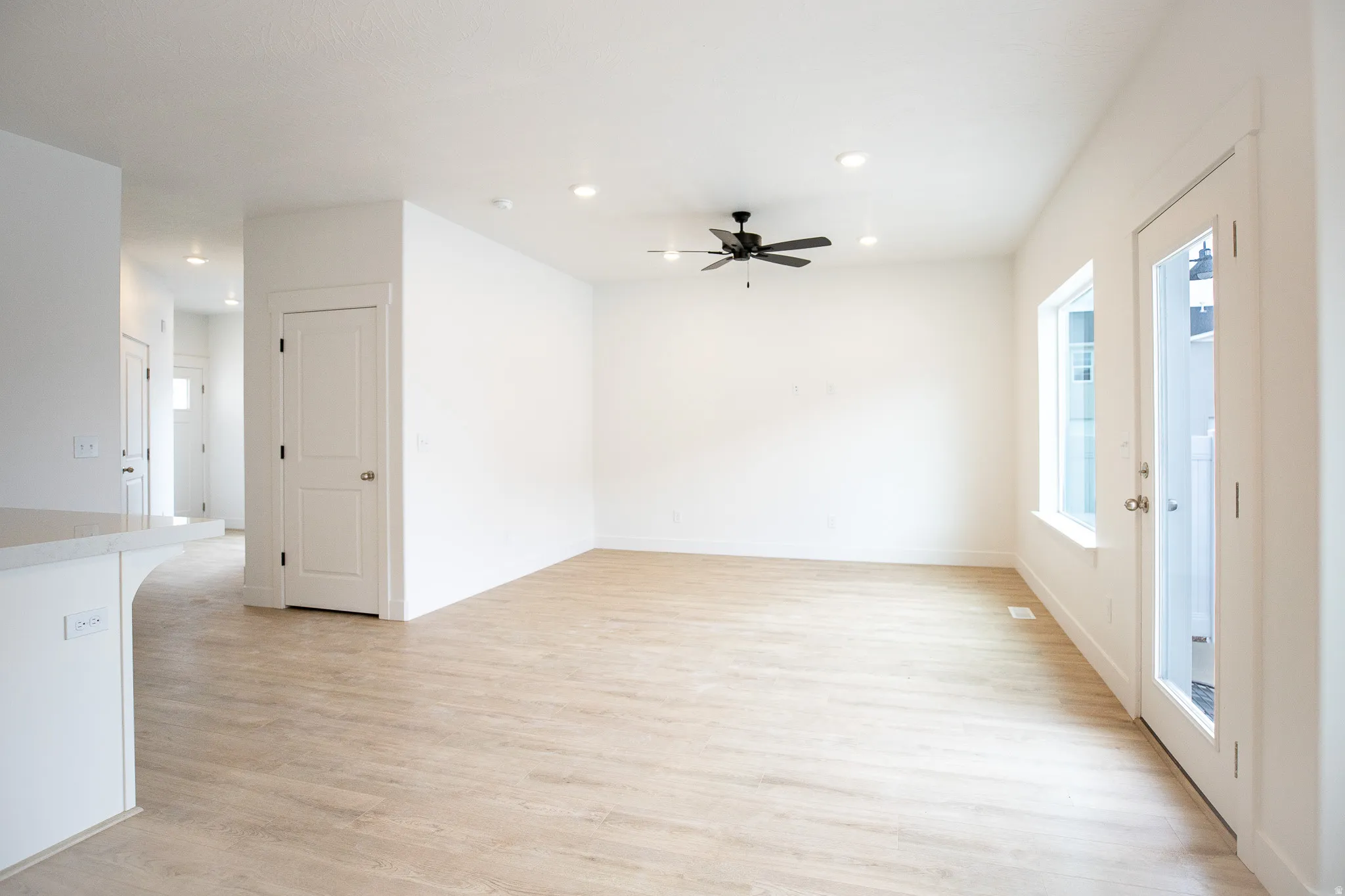 Spacious family room featuring light wood laminate flooring, recessed lighting, and a ceiling fan