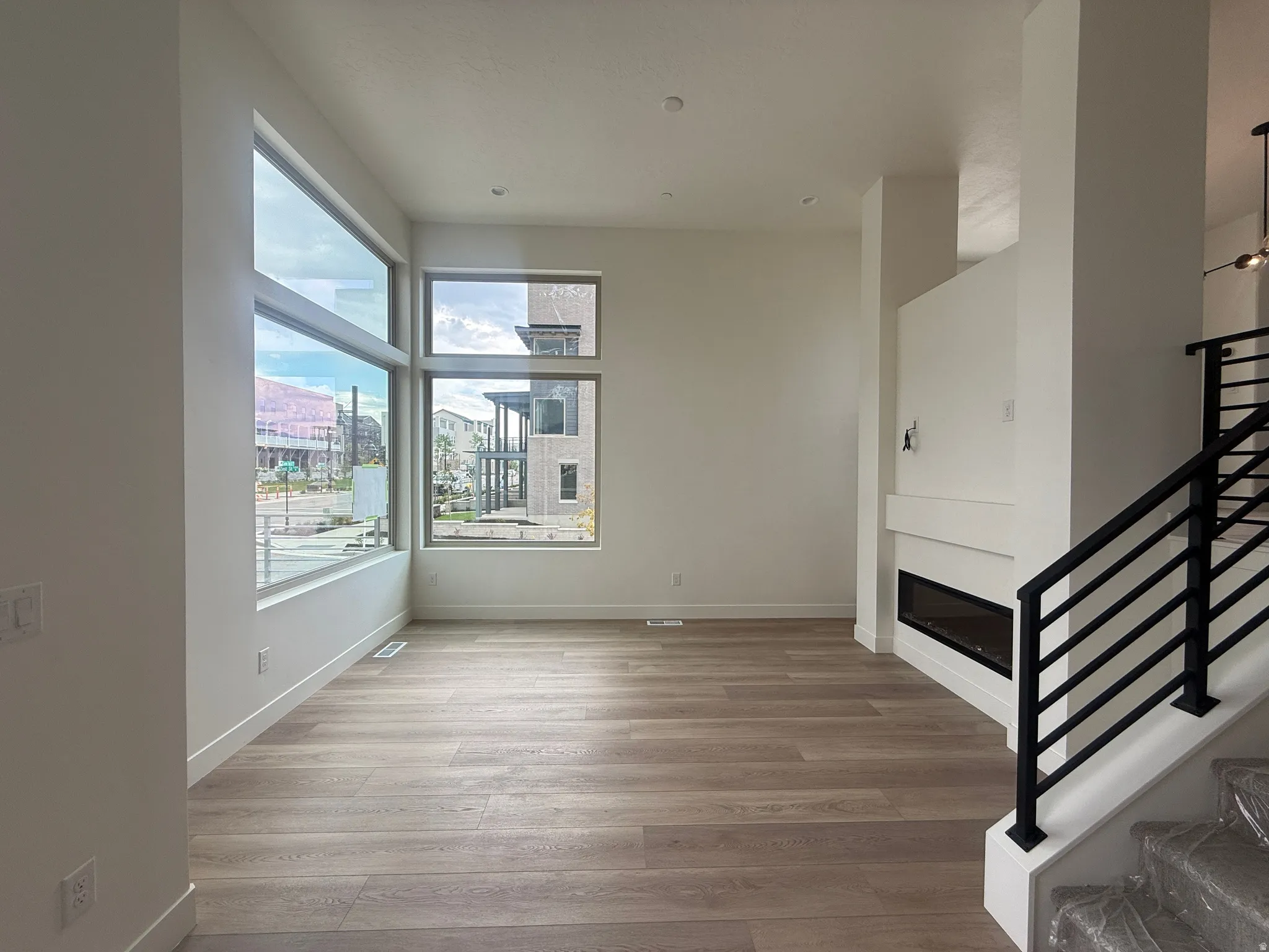 Spacious living area featuring large windows, wood-finish flooring, a contemporary fireplace, and a modern staircase with black metal railings