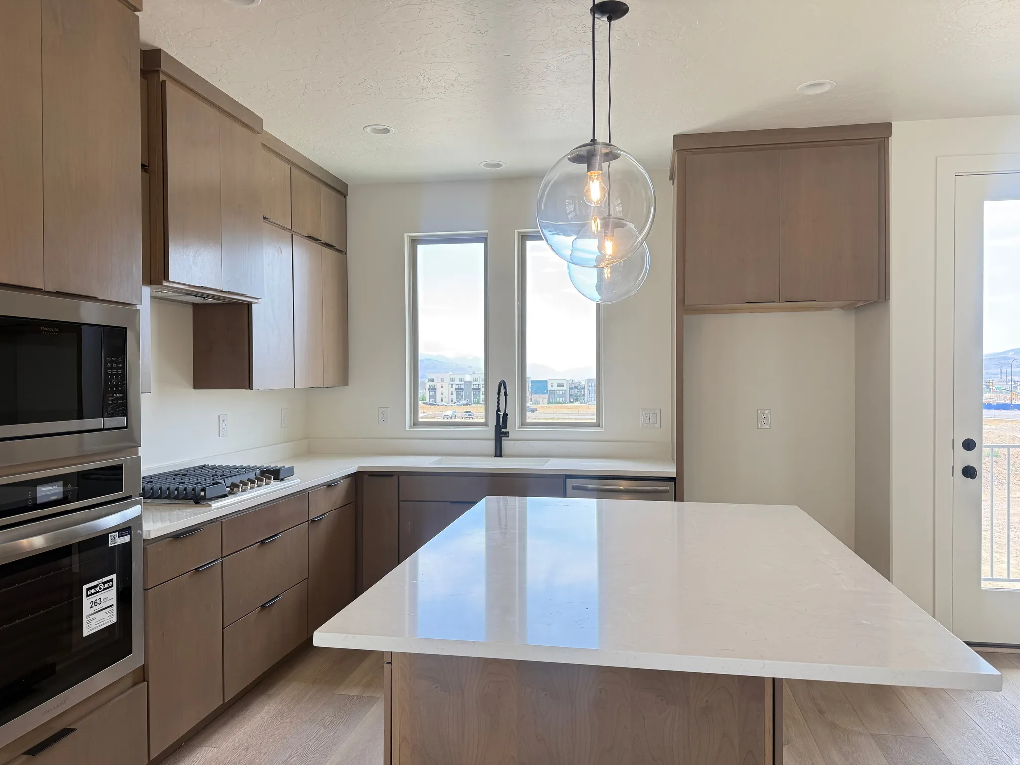 Modern kitchen featuring extensive wood-finish cabinetry, stainless steel appliances, a gas cooktop, and a kitchen island with a light-toned countertop