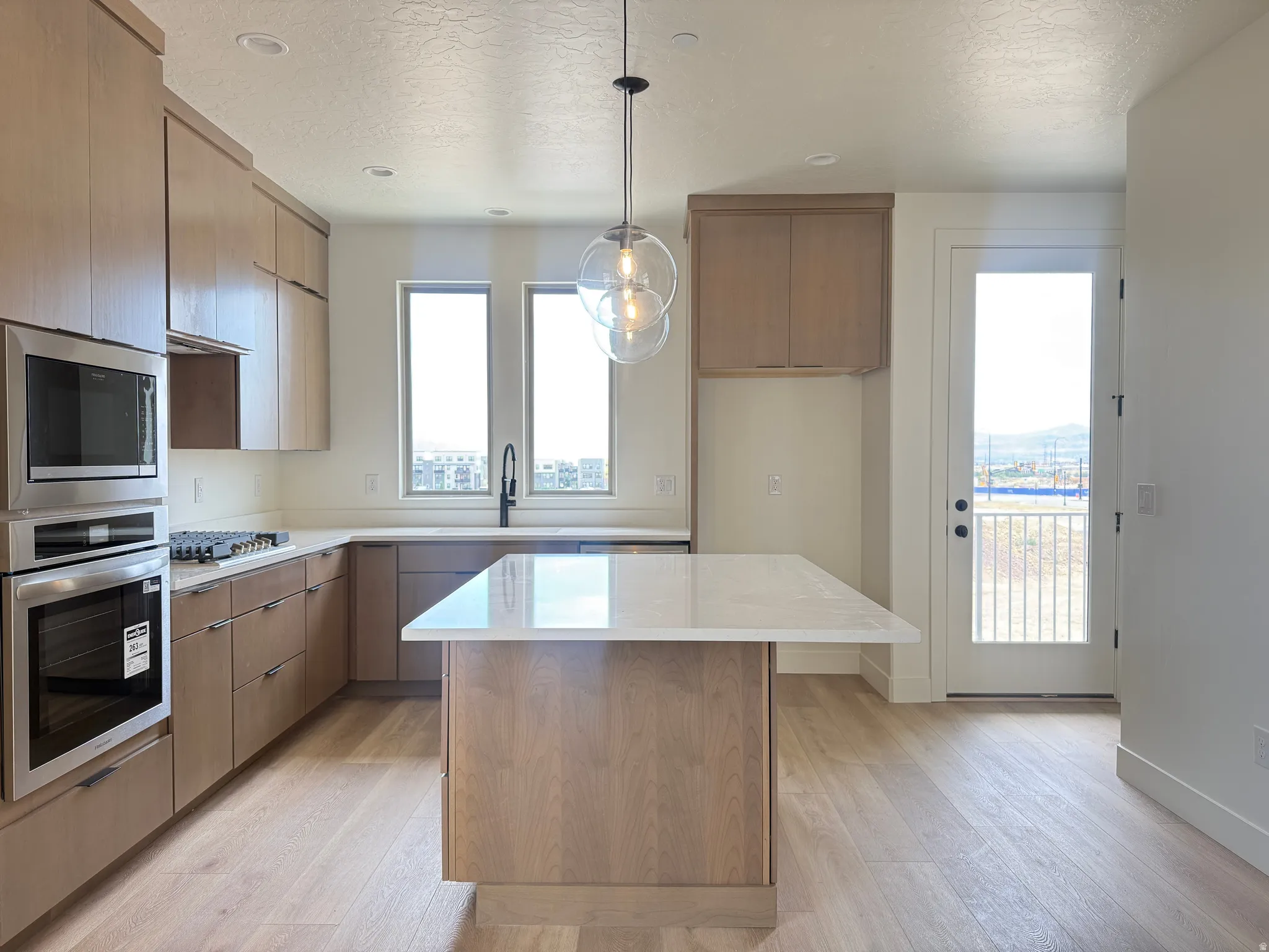 Modern kitchen featuring light wood-finish cabinetry, a large center island with a white countertop, and stainless steel built-in appliances