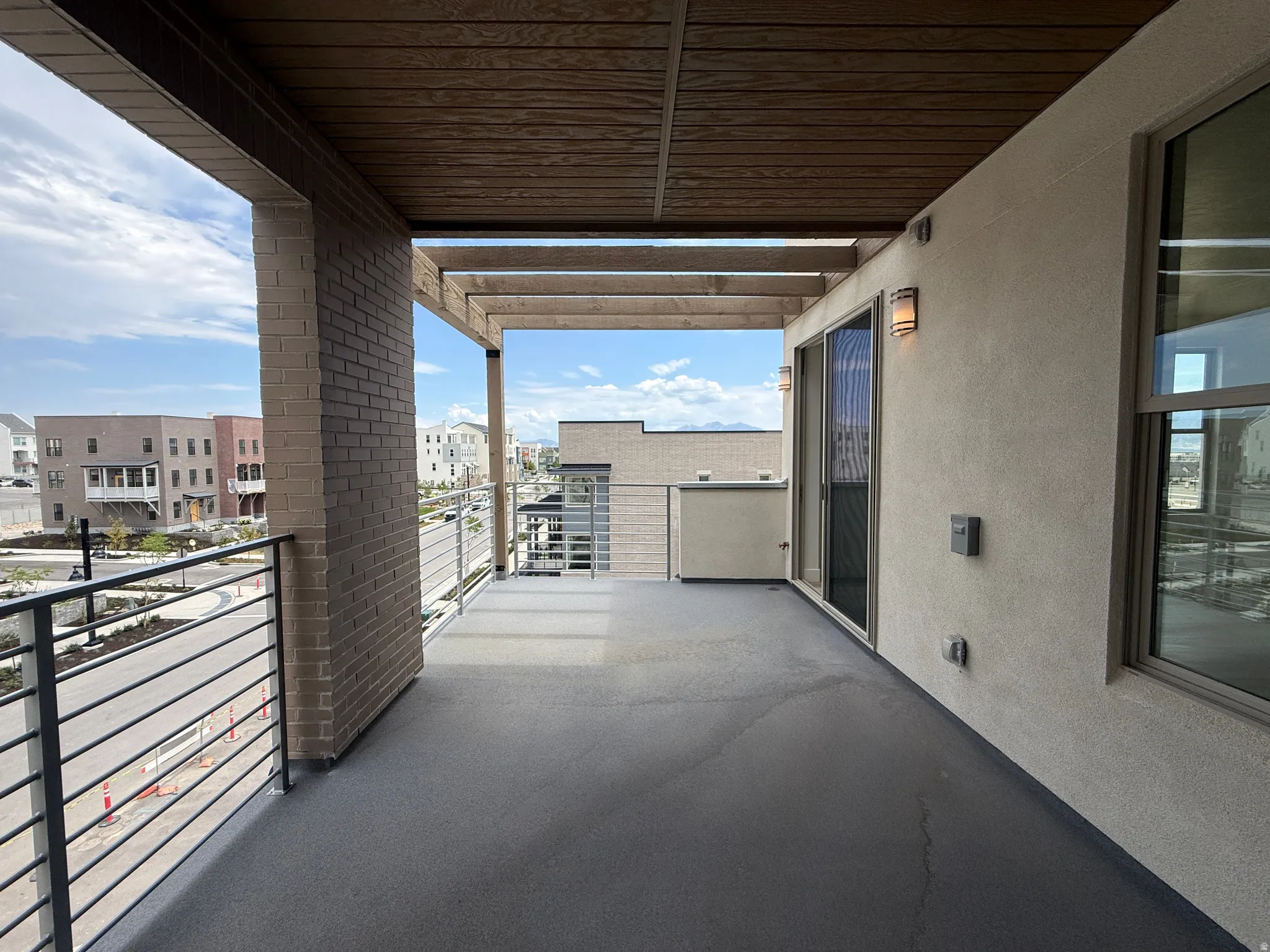 Spacious exterior balcony featuring a wood-finish ceiling, brick pillar, and contemporary metal railings