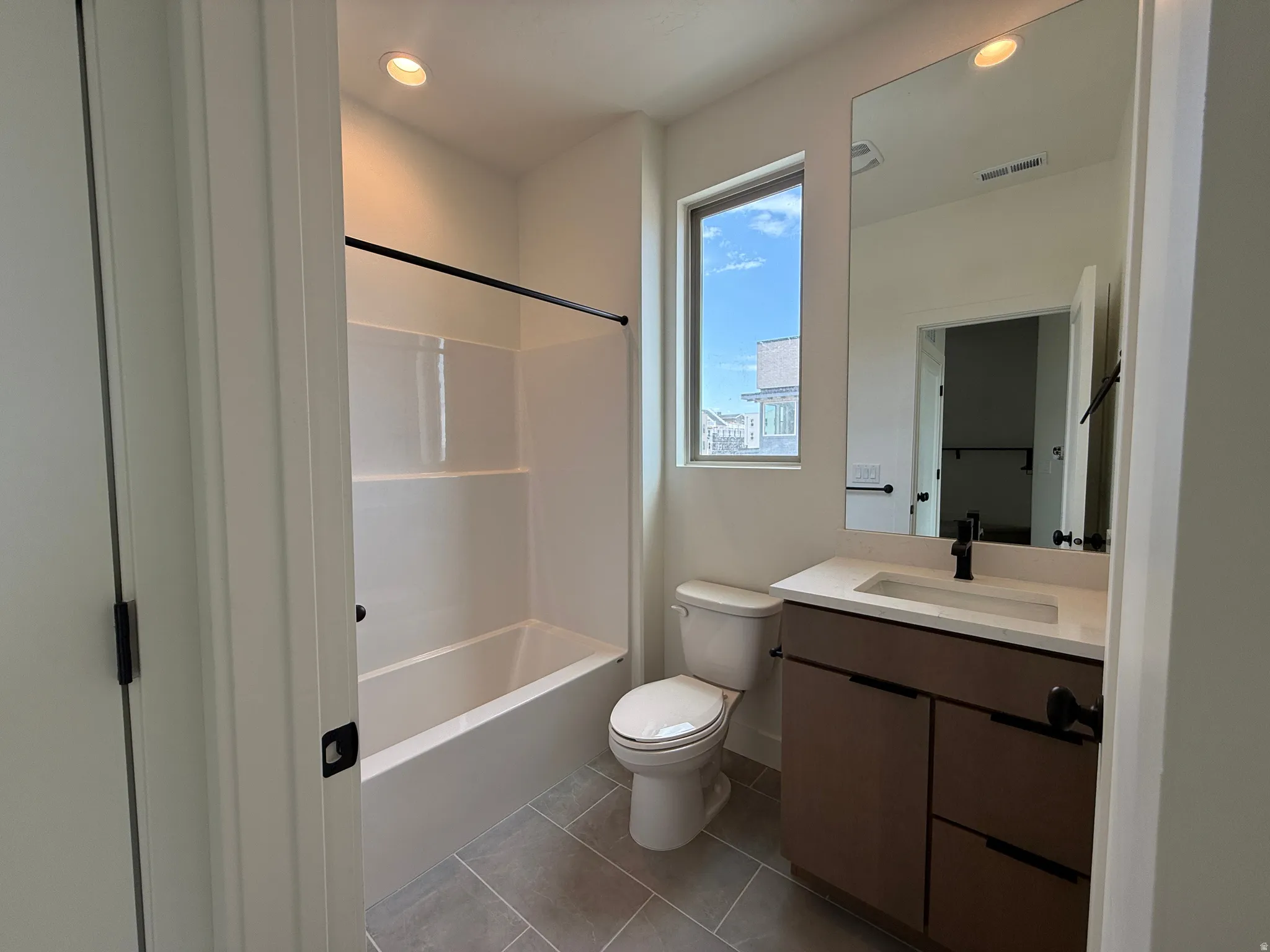 Bathroom featuring a tub/shower combination with a white surround, a toilet, and a vanity with a white countertop and a dark wood-finish cabinet
