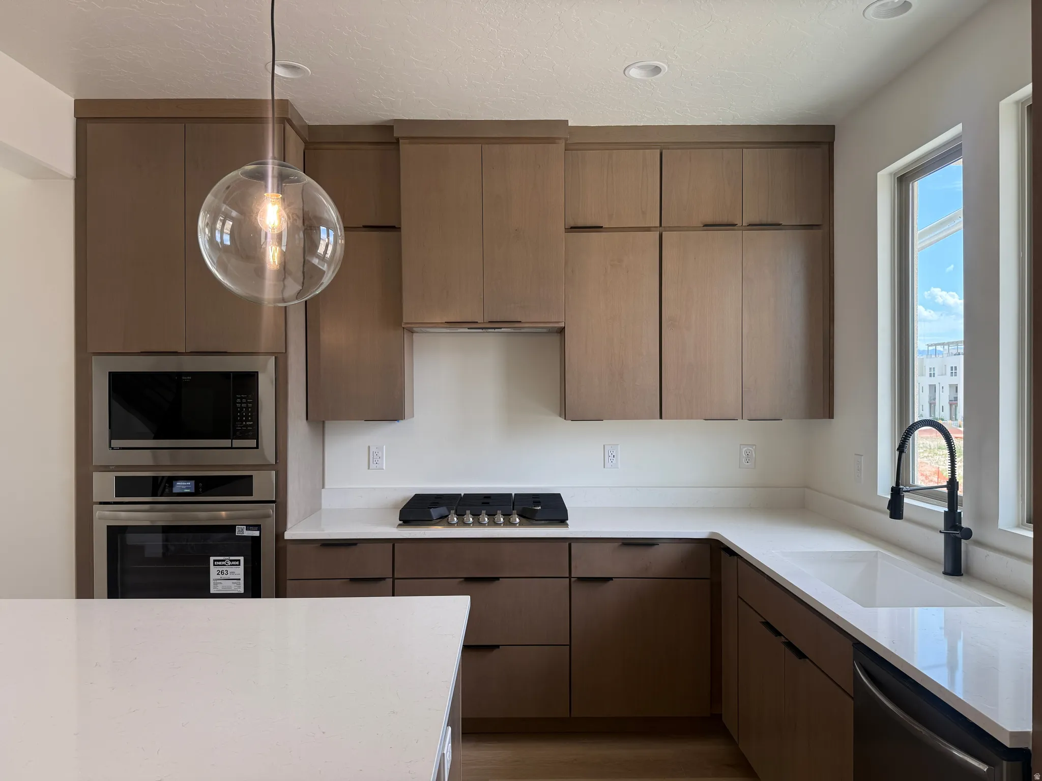 Contemporary kitchen featuring light wood-finish cabinetry, white countertops, and stainless steel appliances