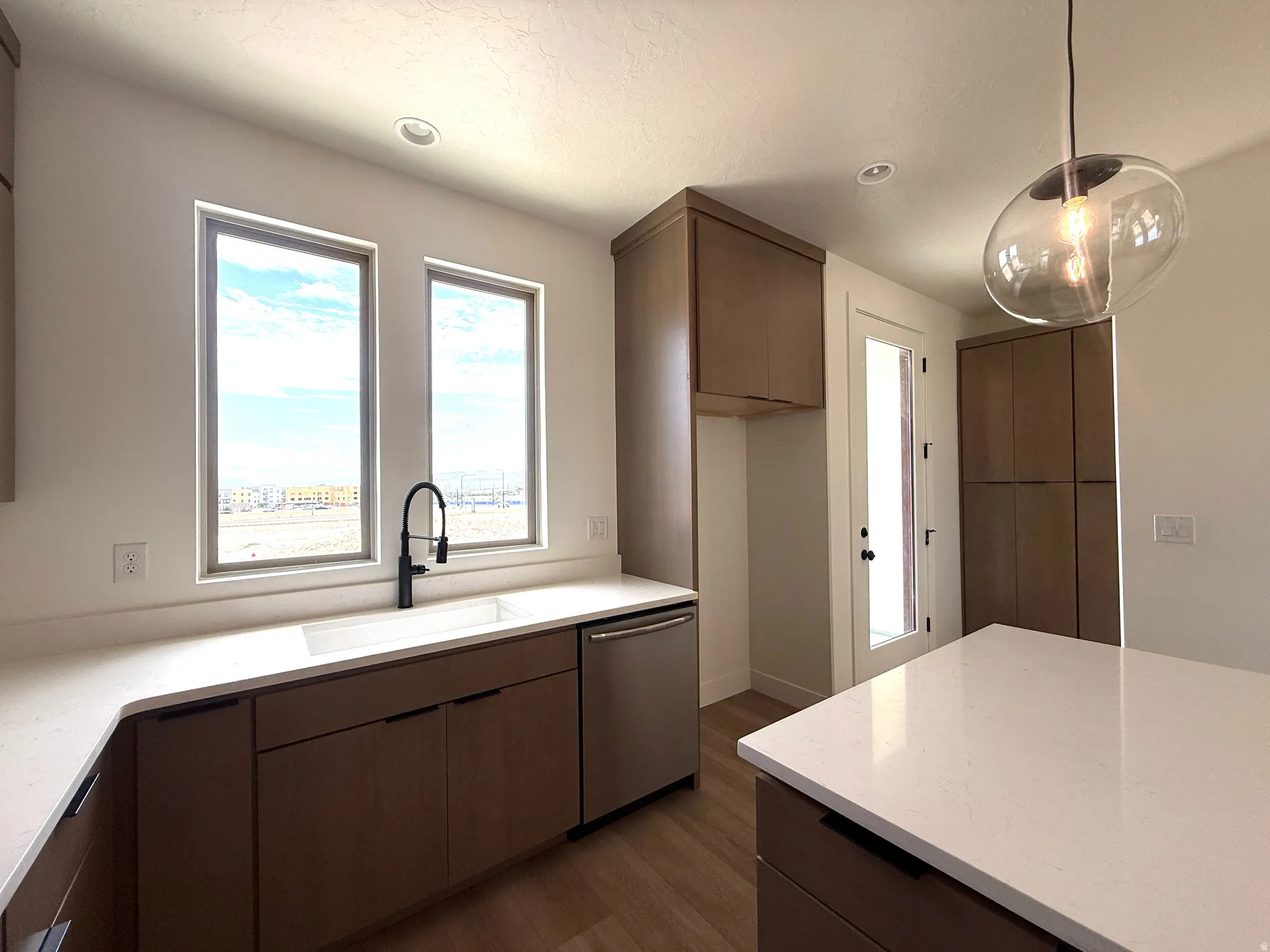Contemporary kitchen featuring a white undermount sink with a matte black faucet, light wood-finish flooring, and white countertops