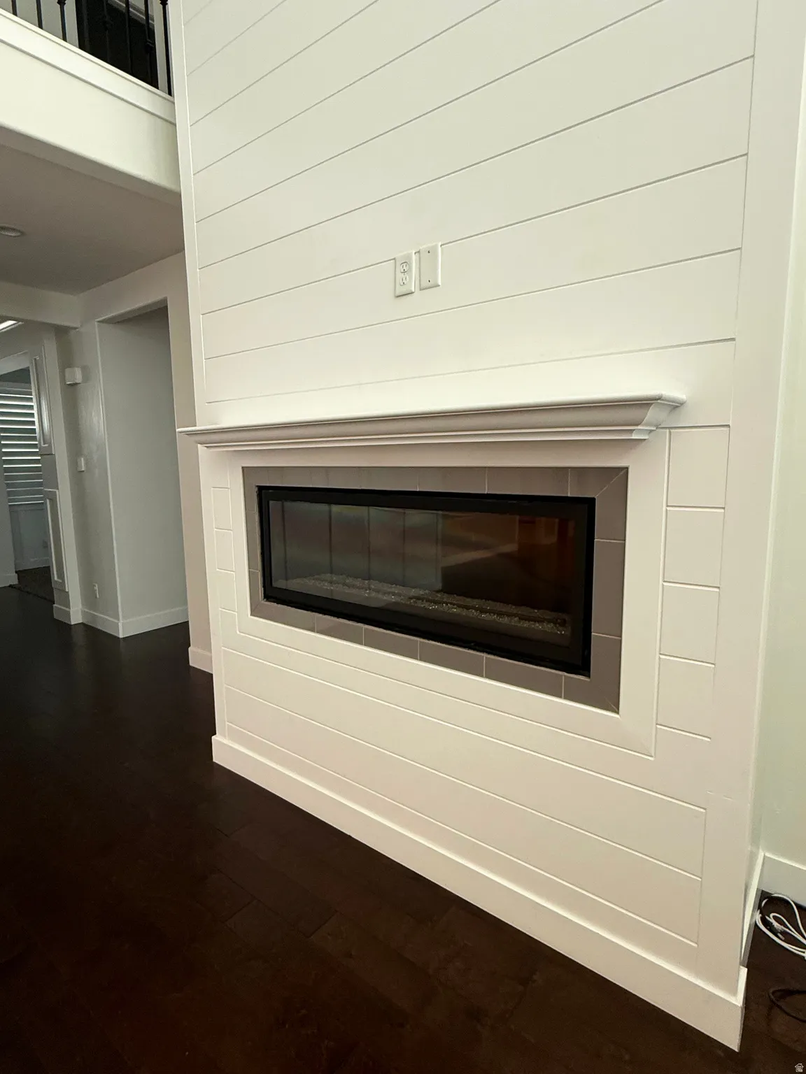 Contemporary fireplace featuring a linear glass-fronted firebox, white shiplap surround, decorative mantel, and dark wood-finish flooring