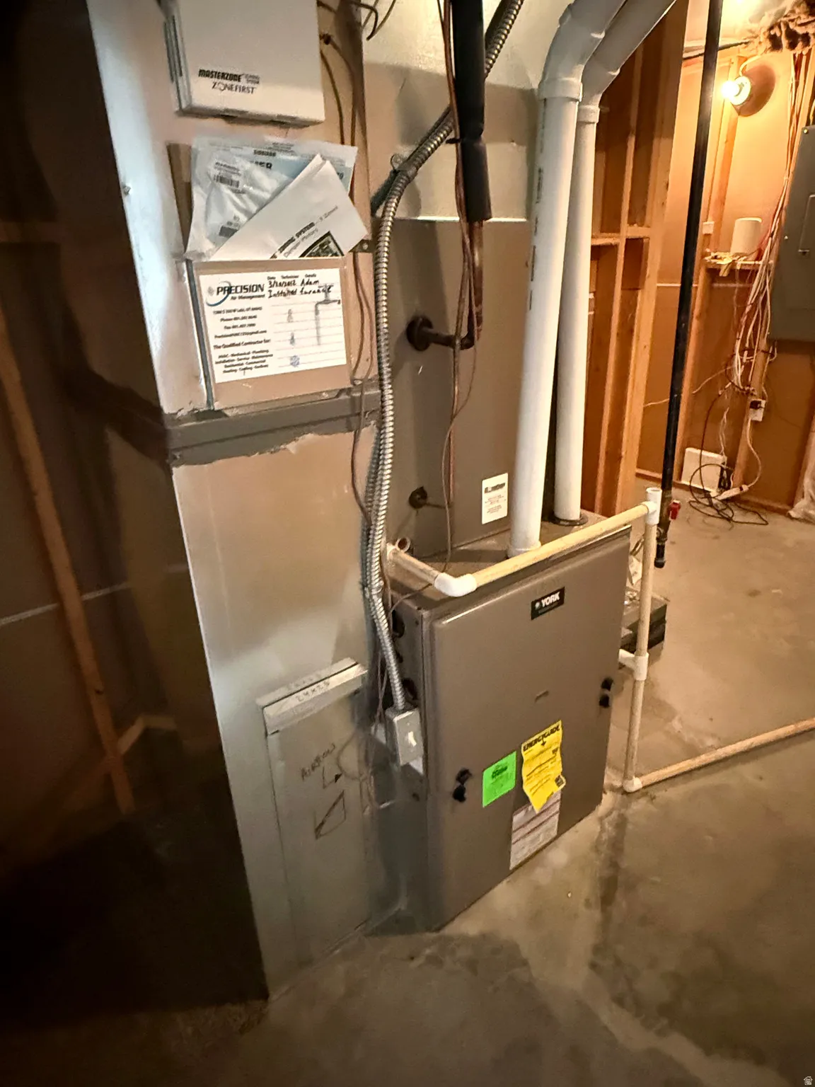 Furnace system with exposed ductwork, PVC piping, and electrical conduit, situated on a concrete floor
