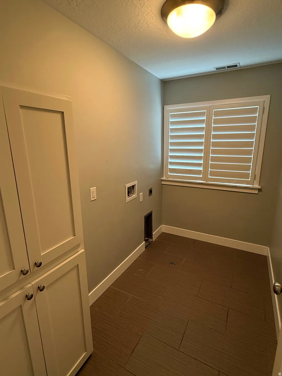 Dedicated utility space featuring built-in cabinetry, wood-look tile flooring, and window shutters