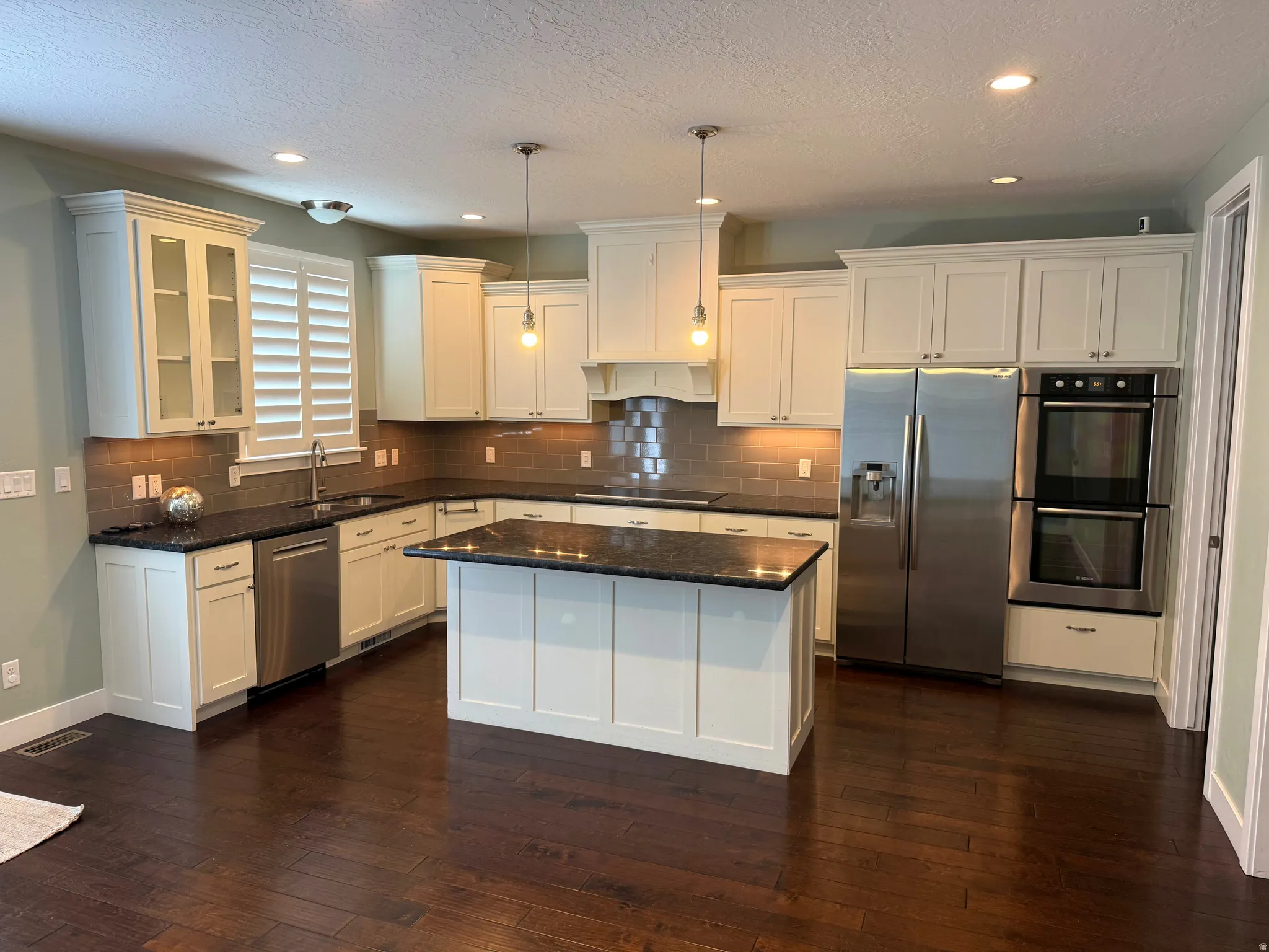 Open-concept kitchen featuring white cabinetry, dark stone countertops, stainless steel appliances, a center island, and wood-finish flooring