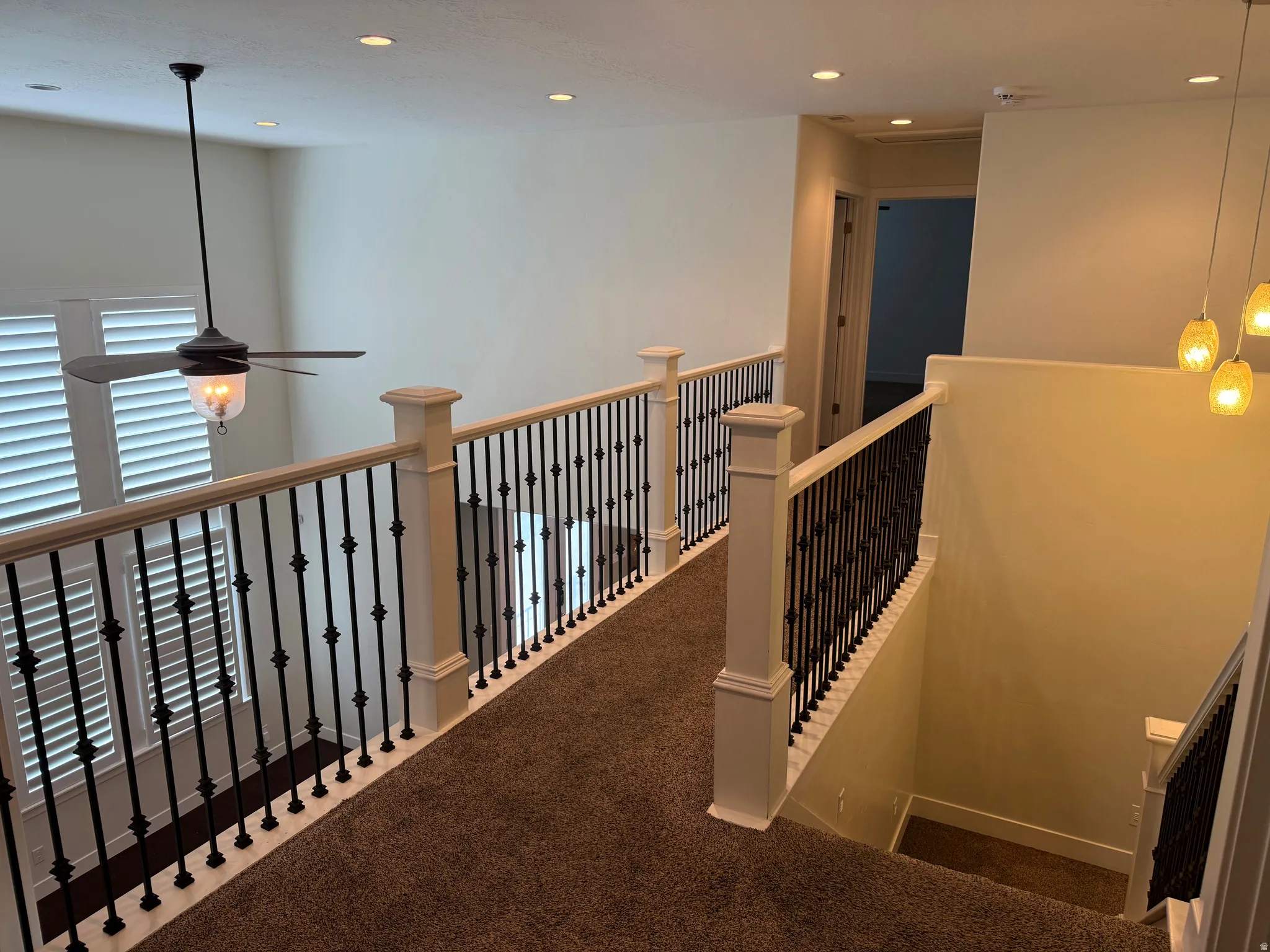 Upper-level landing featuring wrought iron balusters, white newel posts, and recessed ceiling lighting