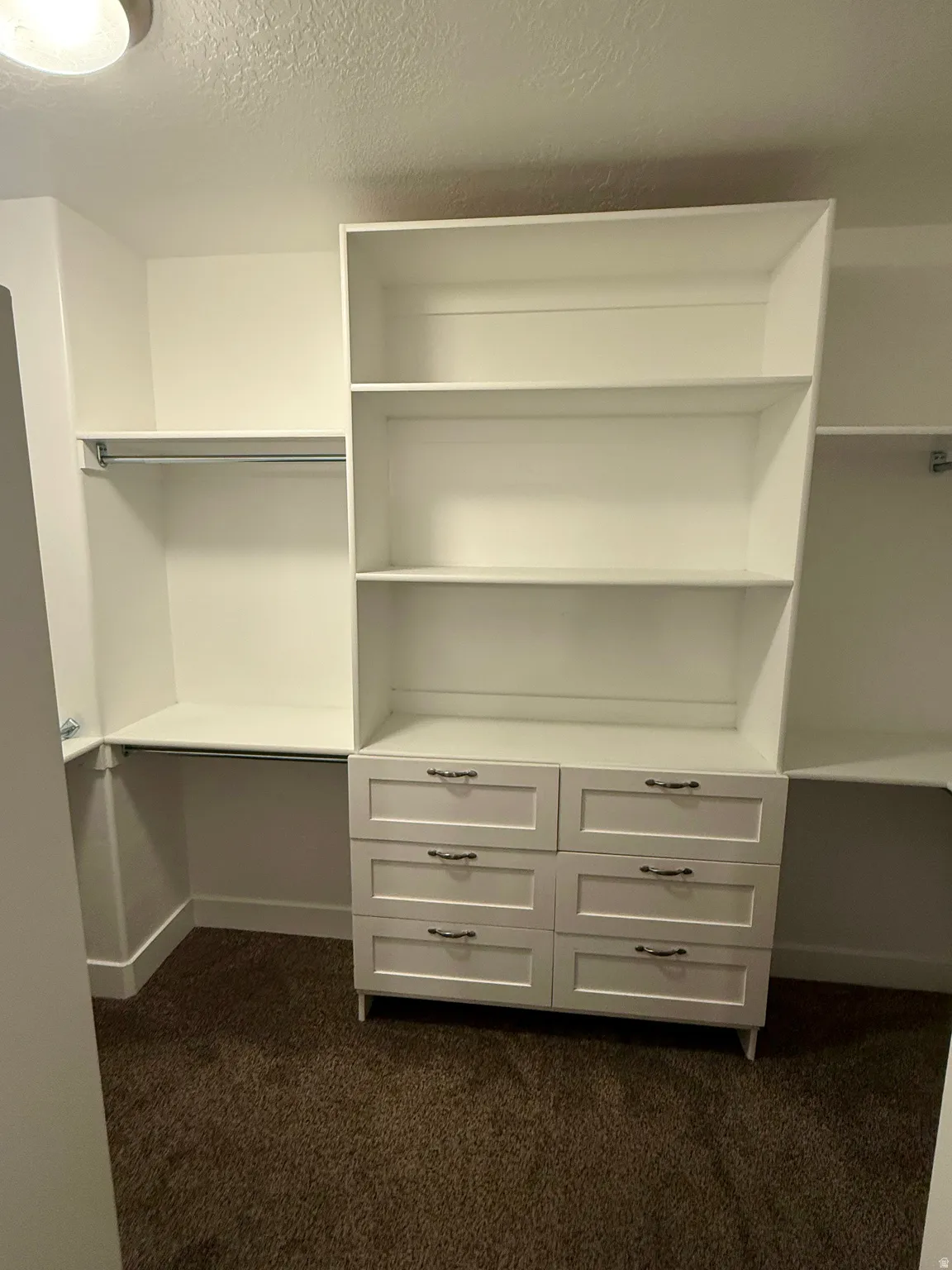 Custom closet system featuring built-in shelving, hanging rods, and a six-drawer dresser with dark hardware