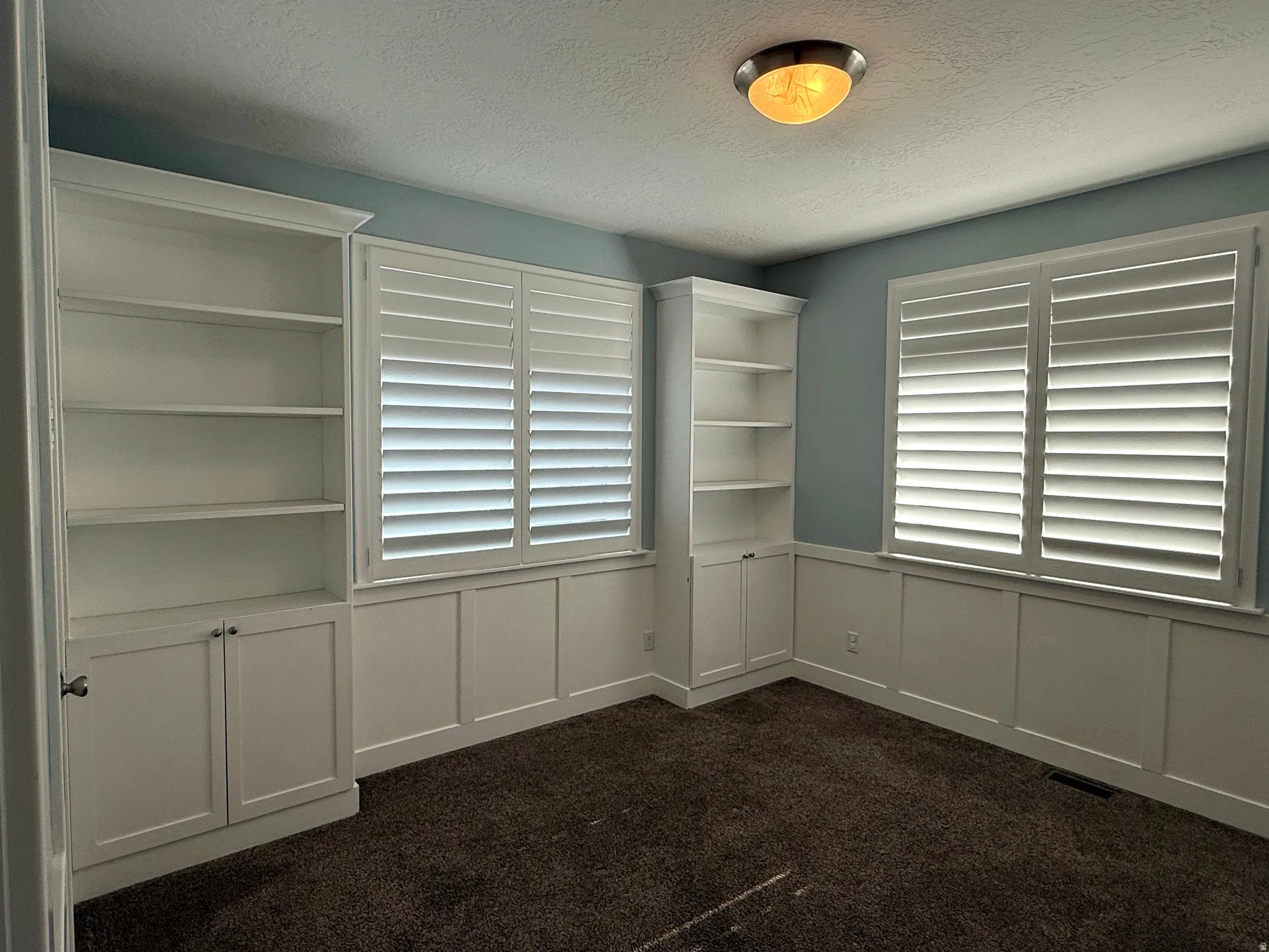 Built-in shelving units flank two windows with plantation shutters