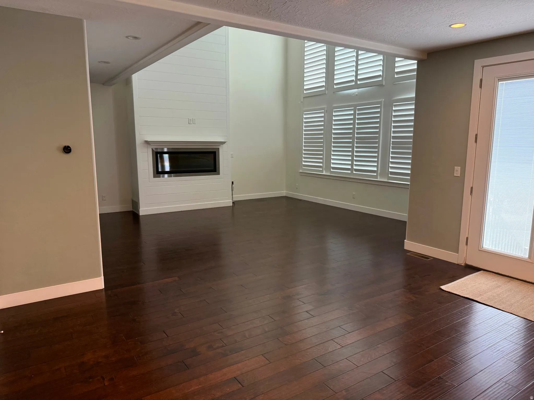 Spacious living area featuring rich wood-finish flooring, a contemporary linear fireplace with shiplap surround, and soaring ceilings