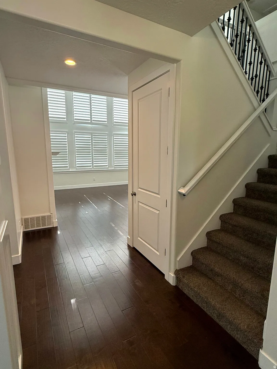 Entryway featuring dark wood-finish flooring, a carpeted staircase with an ornamental wrought iron railing, and a paneled door