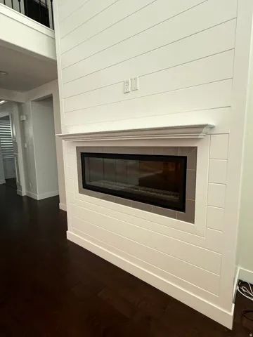 Contemporary fireplace featuring a linear glass-fronted firebox, white shiplap surround, decorative mantel, and dark wood-finish flooring