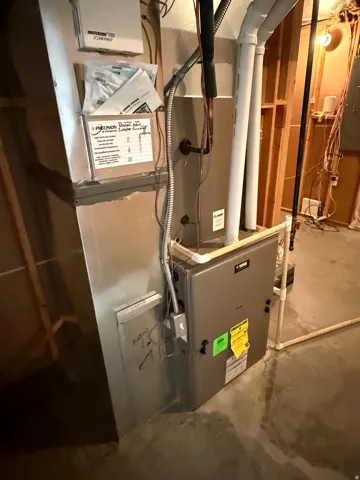 Furnace system with exposed ductwork, PVC piping, and electrical conduit, situated on a concrete floor