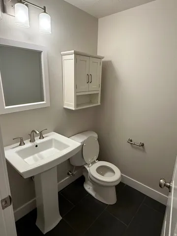 Powder room featuring a pedestal sink with brushed nickel fixtures, a white framed mirror, and dark tile flooring
