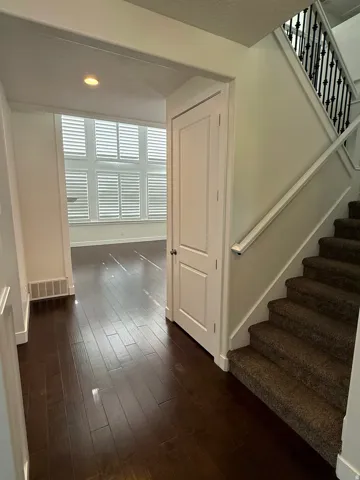 Entryway featuring dark wood-finish flooring, a carpeted staircase with an ornamental wrought iron railing, and a paneled door
