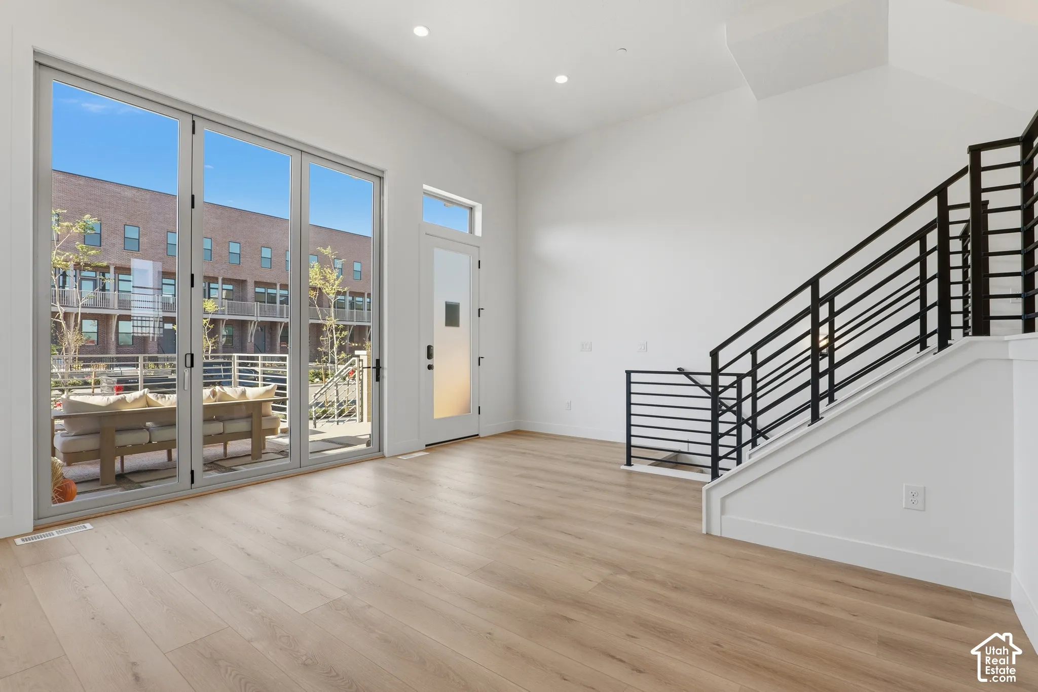 Open-concept interior featuring wood-finish flooring, floor-to-ceiling glass sliding doors, recessed lighting, and a staircase with matte black horizontal railings