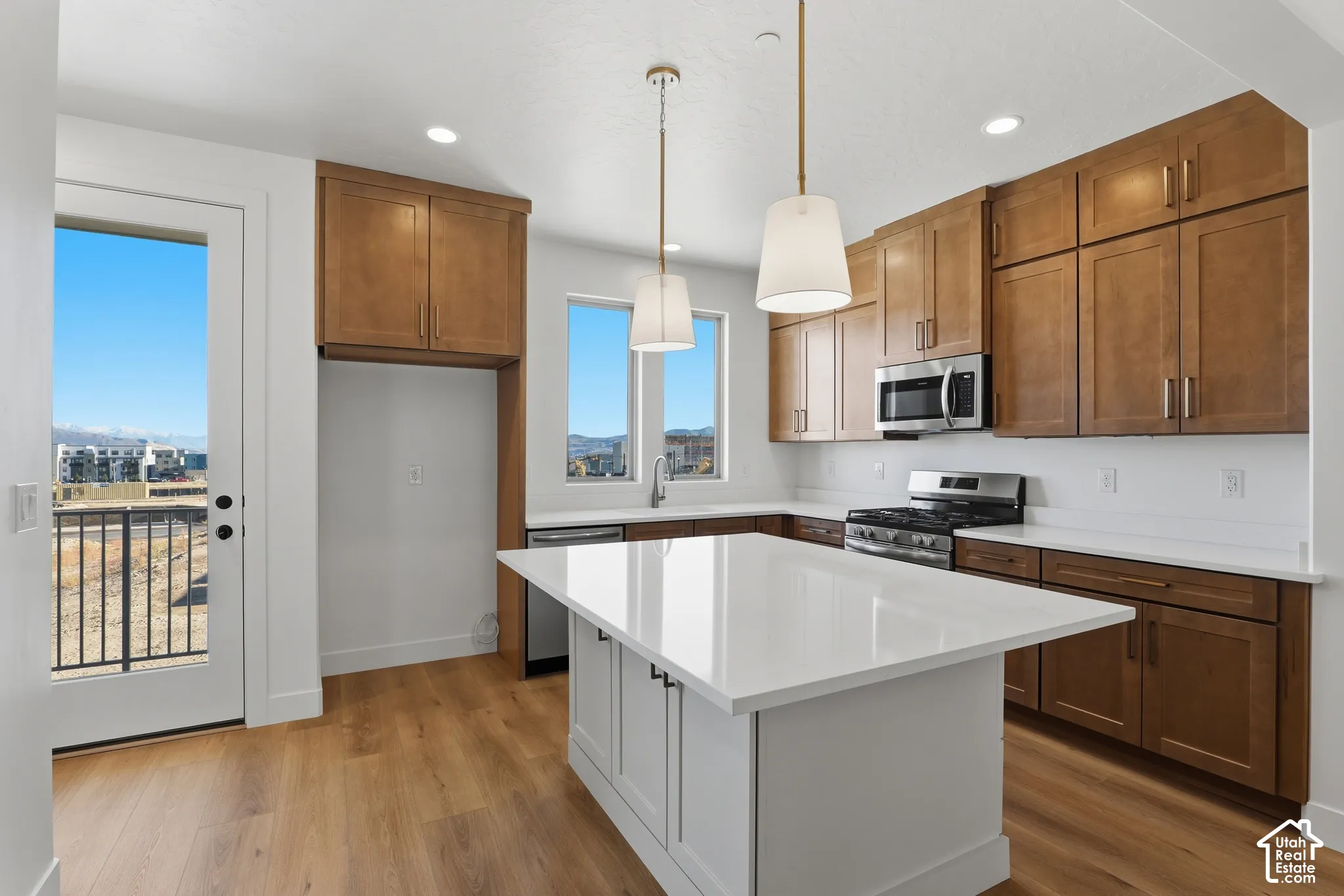 Kitchen featuring warm-toned wood cabinetry, an oversized central island with a quartz countertop, wood-finish flooring, stainless steel appliances, and dual pendant lighting