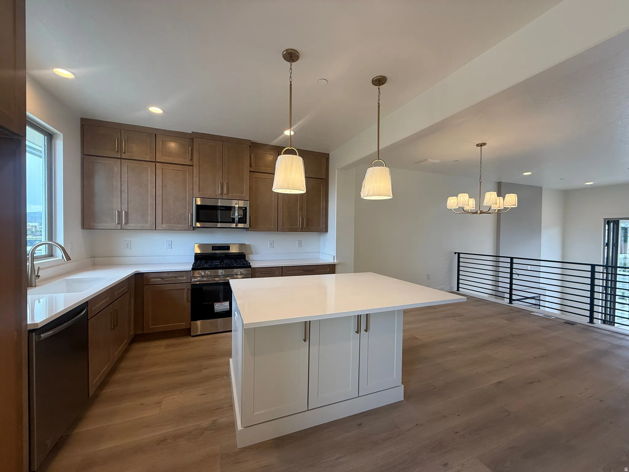Modern kitchen featuring a white countertop island, stainless steel appliances, wood-finish flooring, and recessed lighting